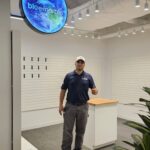 Electrician in modern retail space under round LED sign — evenly spaced track lighting